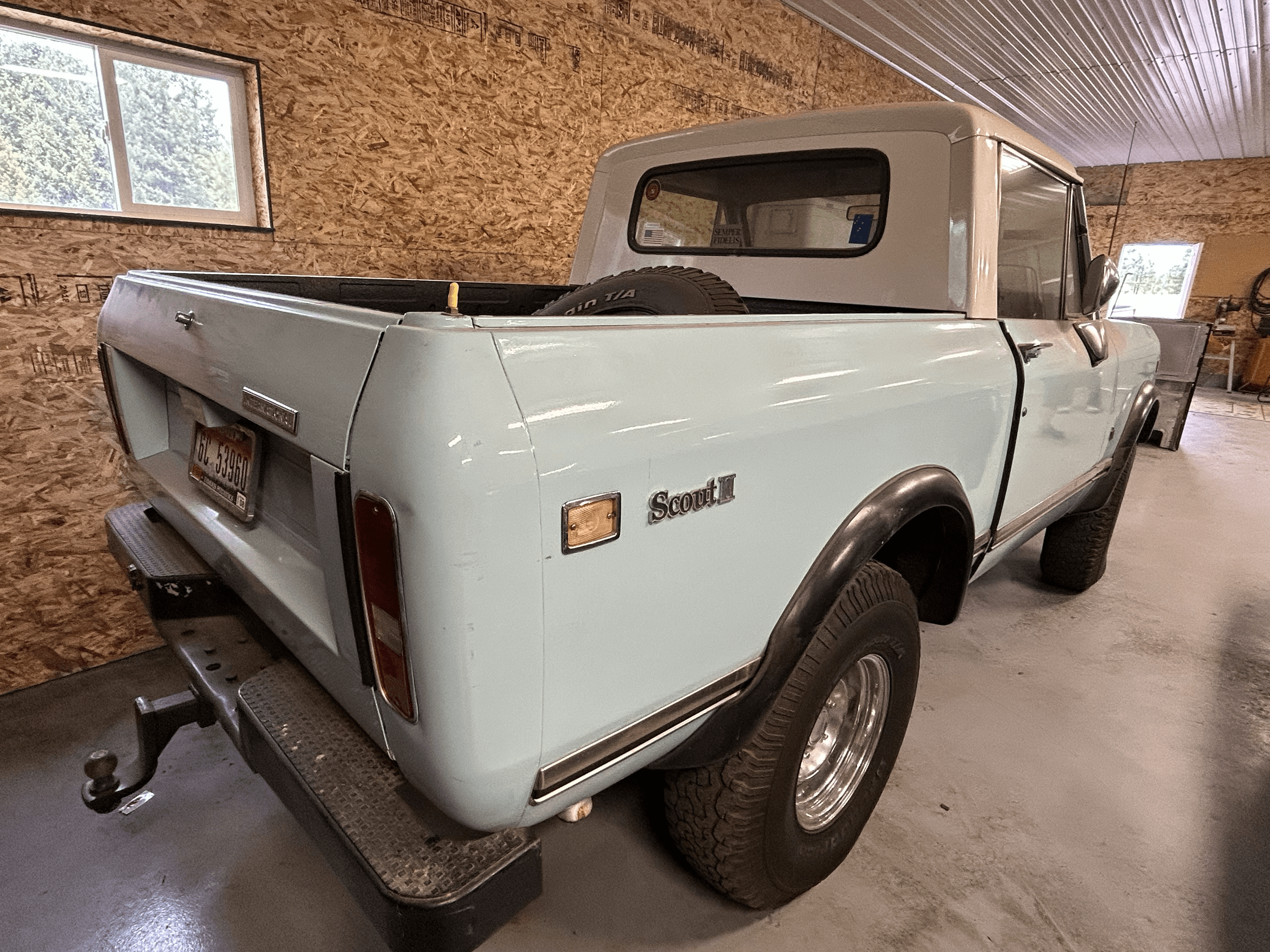 Light blue International Harvester Scout II truck parked inside a garage with plywood walls.