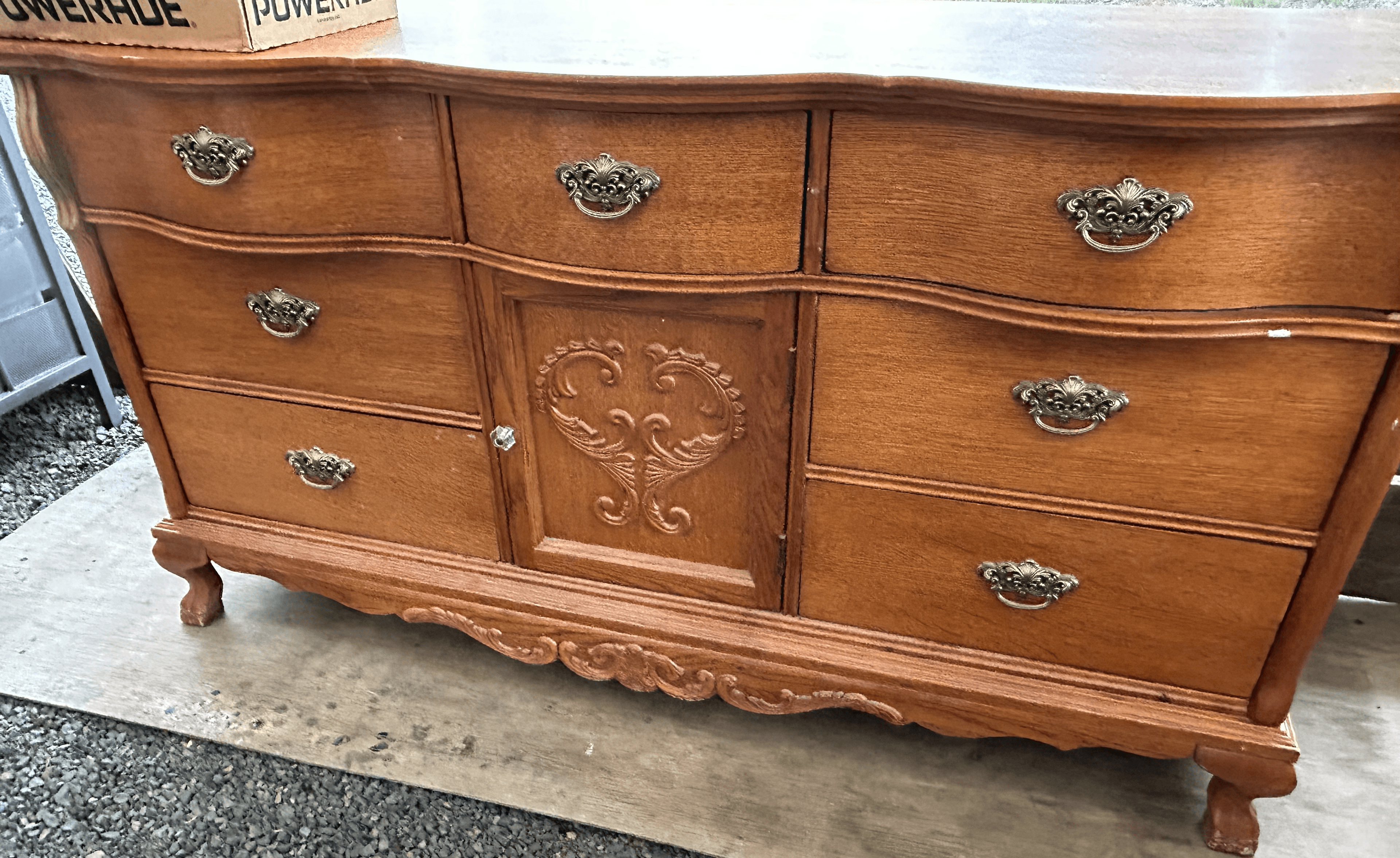 Vintage wooden dresser with ornate metal handles and a central cabinet door with decorative carving.